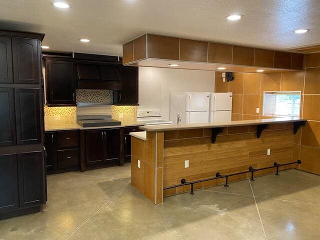 kitchen featuring a kitchen bar, decorative backsplash, light countertops, and freestanding refrigerator