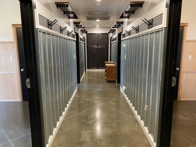 corridor featuring concrete flooring, a wainscoted wall, and wooden walls