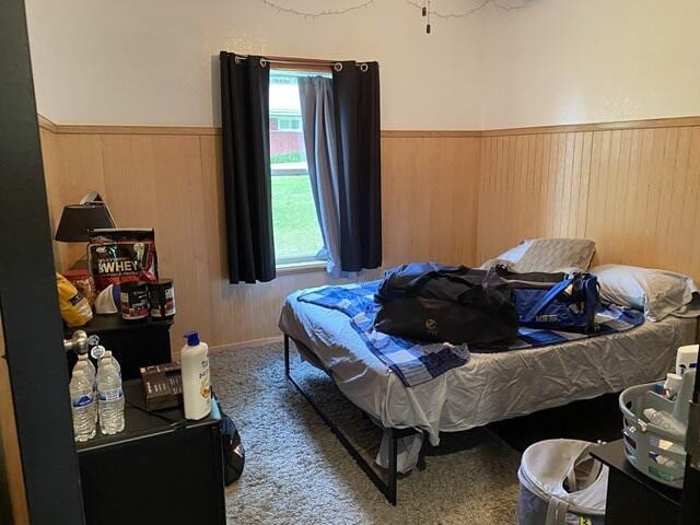 bedroom featuring wainscoting, wood walls, and carpet flooring