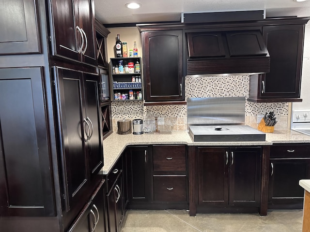 kitchen with light stone counters, custom exhaust hood, open shelves, tasteful backsplash, and dark brown cabinets