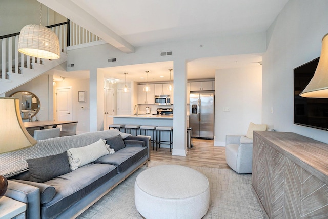 living area featuring beam ceiling, visible vents, light wood-style flooring, and baseboards