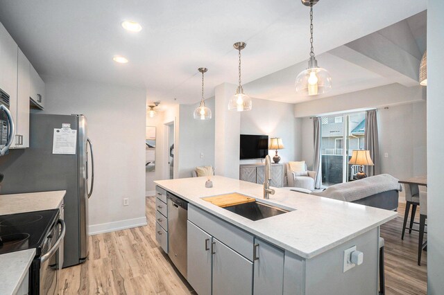 kitchen with an island with sink, open floor plan, decorative light fixtures, light countertops, and a sink