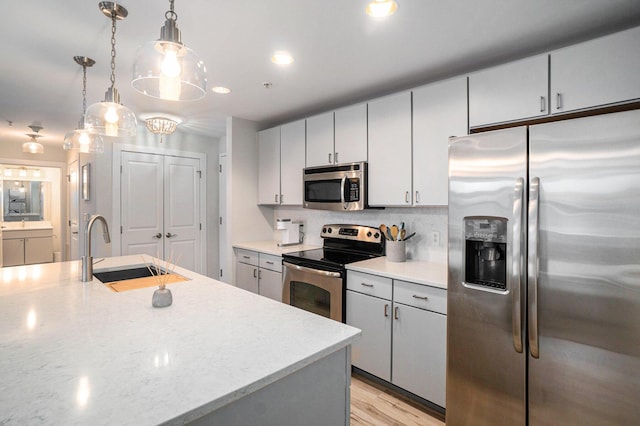 kitchen featuring hanging light fixtures, gray cabinets, stainless steel appliances, light wood-style floors, and a sink