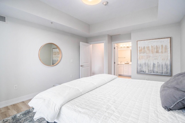 bedroom with a raised ceiling, visible vents, ensuite bathroom, light wood-style floors, and baseboards