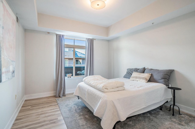 bedroom with a tray ceiling, baseboards, visible vents, and light wood finished floors