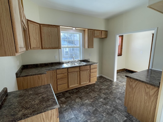 kitchen featuring dark countertops, stone finish flooring, a sink, and baseboards