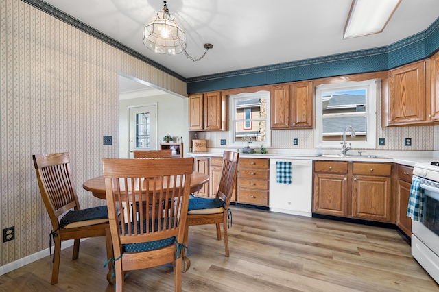 kitchen with light countertops, a sink, light wood-type flooring, white appliances, and wallpapered walls