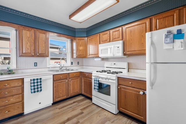 kitchen featuring light wood finished floors, white appliances, a sink, and brown cabinets