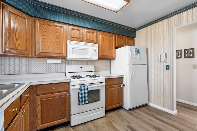 kitchen with brown cabinetry, white appliances, light wood-style floors, and wallpapered walls