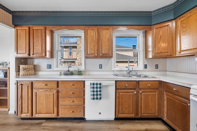 kitchen featuring white dishwasher, light wood-style flooring, a sink, brown cabinets, and wallpapered walls