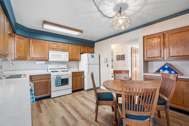 kitchen featuring white appliances, a sink, light countertops, light wood finished floors, and wallpapered walls