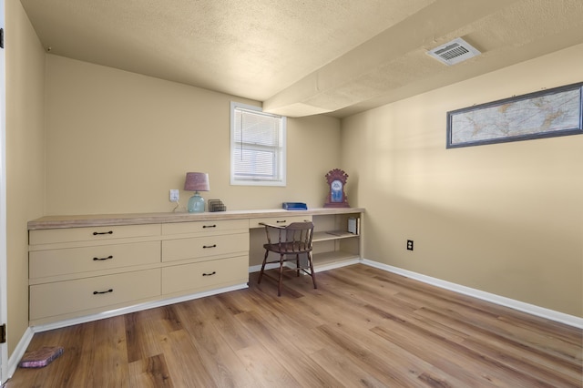 office space featuring baseboards, light wood-style flooring, visible vents, and a textured ceiling