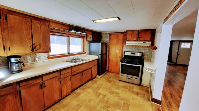 kitchen with stainless steel gas stove, freestanding refrigerator, light countertops, under cabinet range hood, and a sink