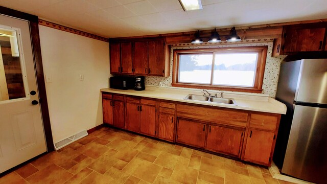 kitchen with visible vents, light countertops, a sink, and freestanding refrigerator