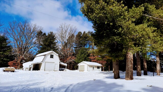 yard layered in snow featuring a garage and an outbuilding