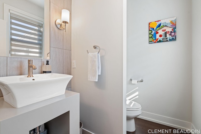 half bath with toilet, baseboards, wood finished floors, and vanity