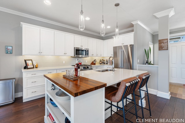 kitchen featuring stainless steel appliances, a sink, wooden counters, ornamental molding, and an island with sink