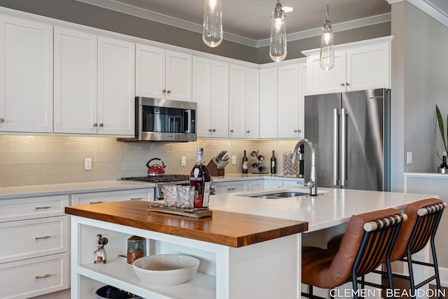 kitchen with a kitchen island with sink, stainless steel appliances, wood counters, open shelves, and crown molding