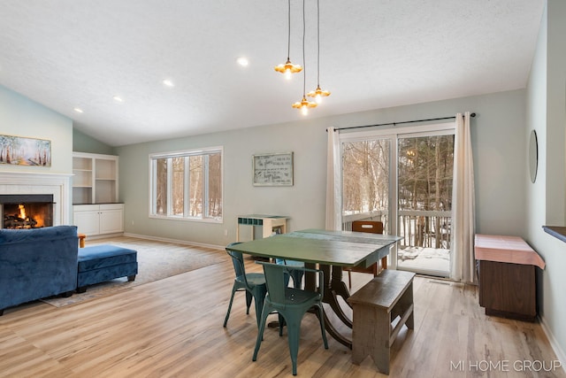 dining room featuring light wood finished floors, baseboards, vaulted ceiling, a textured ceiling, and a fireplace