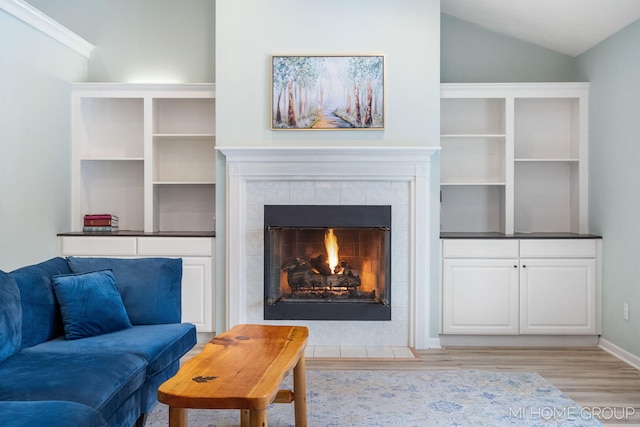 living area with lofted ceiling, a tiled fireplace, light wood-style flooring, and baseboards