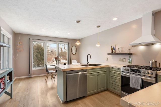 kitchen featuring wall chimney exhaust hood, appliances with stainless steel finishes, a peninsula, pendant lighting, and a sink