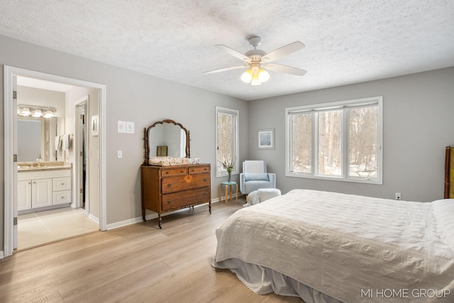 bedroom featuring light wood-style flooring, a ceiling fan, a textured ceiling, ensuite bath, and baseboards