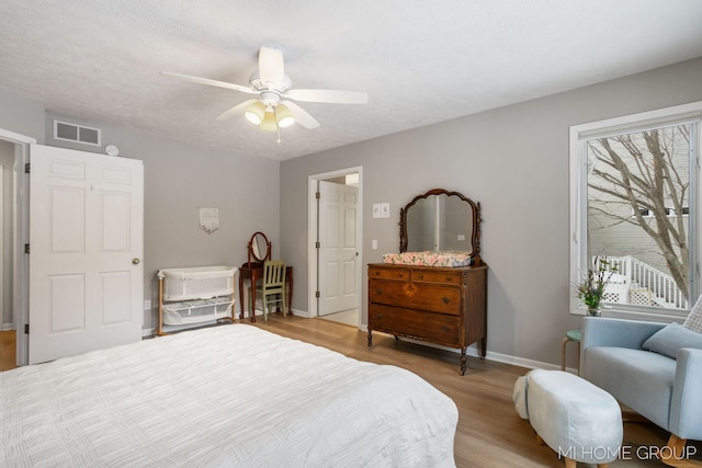 bedroom with a textured ceiling, a ceiling fan, visible vents, baseboards, and light wood-type flooring