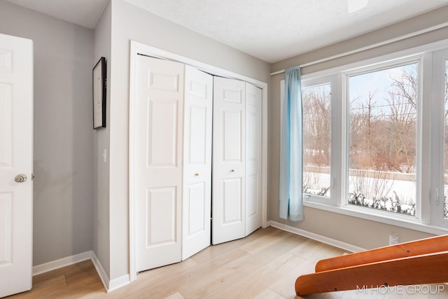 unfurnished bedroom featuring a textured ceiling, a closet, light wood-type flooring, and baseboards