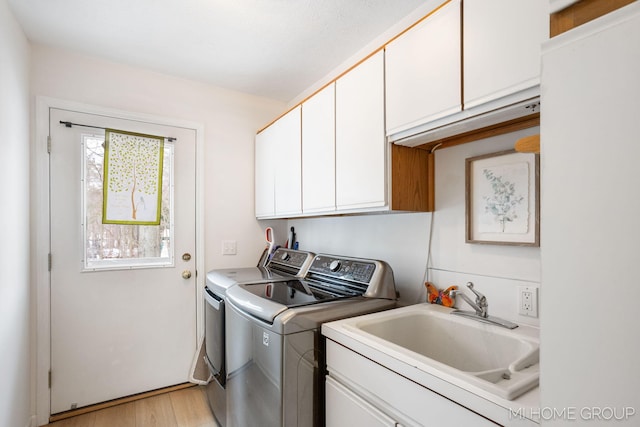 laundry room featuring cabinet space, a sink, light wood finished floors, and separate washer and dryer