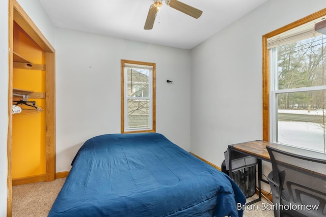 bedroom featuring light carpet, multiple windows, baseboards, and a ceiling fan