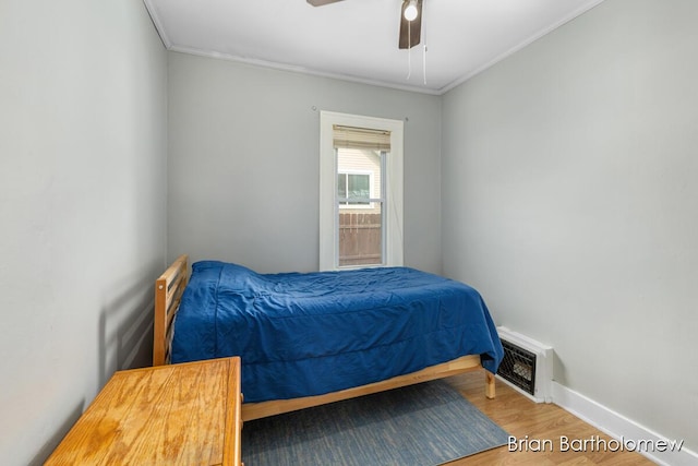 bedroom with wood finished floors, a ceiling fan, baseboards, visible vents, and crown molding