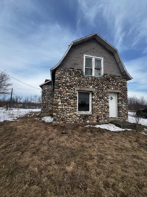 snow covered property featuring stone siding and a gambrel roof