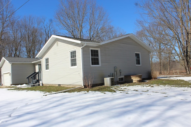 view of snowy exterior featuring an attached garage and cooling unit