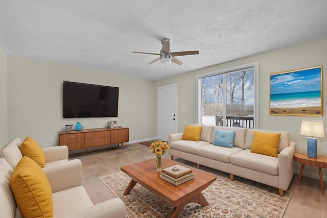 living room featuring light wood-style flooring, baseboards, ceiling fan, and a textured ceiling