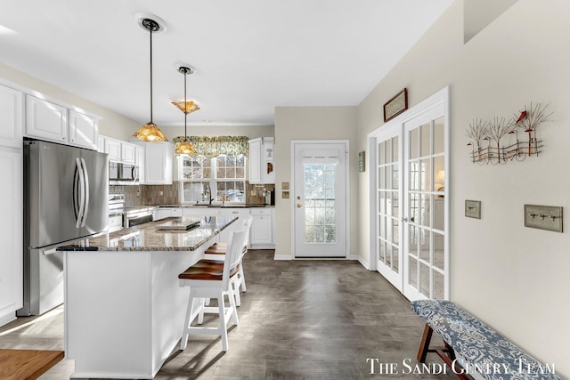 kitchen featuring a center island, decorative backsplash, appliances with stainless steel finishes, white cabinetry, and light stone countertops