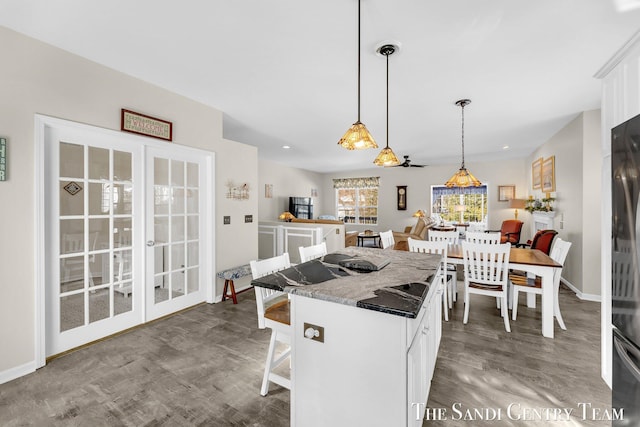 kitchen featuring a breakfast bar area, a kitchen island, wood finished floors, white cabinetry, and decorative light fixtures