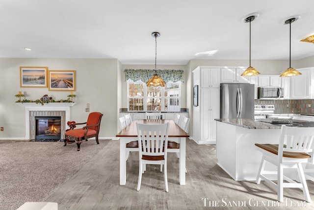 dining space with light wood finished floors, baseboards, and a tiled fireplace