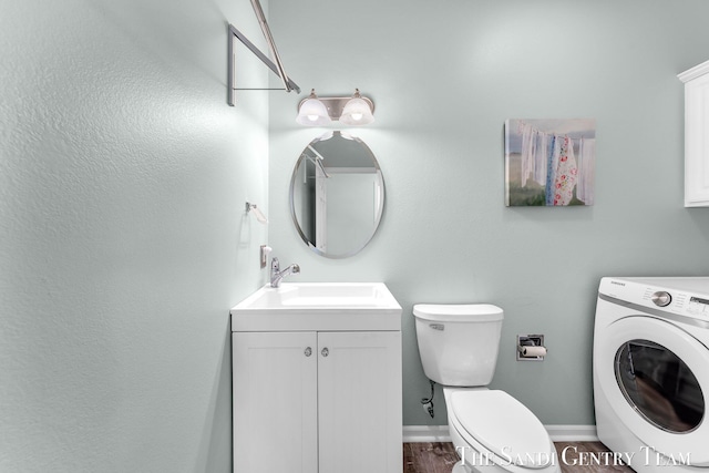 bathroom featuring baseboards, toilet, washer / clothes dryer, wood finished floors, and vanity