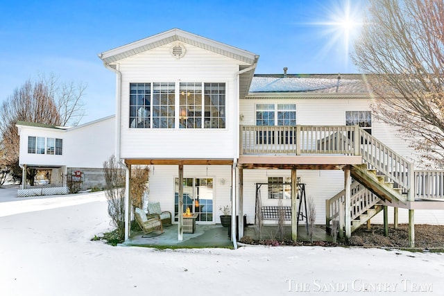 snow covered rear of property with stairs and a patio area