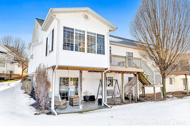 snow covered back of property featuring stairs