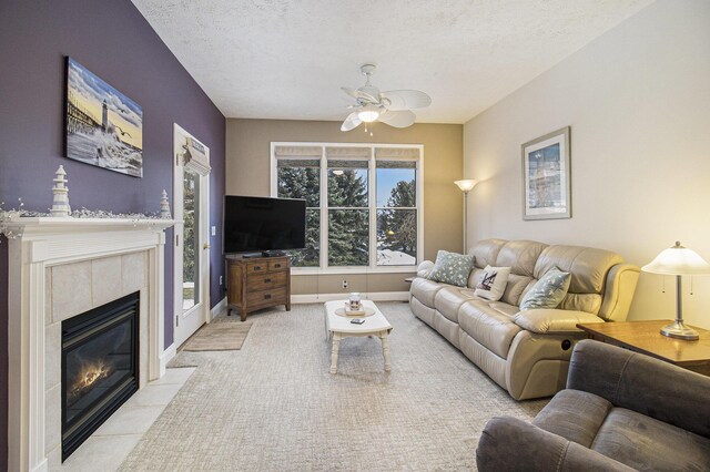 living room with a textured ceiling, ceiling fan, a tile fireplace, light colored carpet, and baseboards