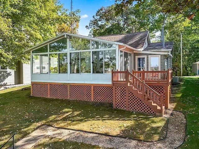 back of property featuring a lawn, a sunroom, roof with shingles, stairs, and a deck