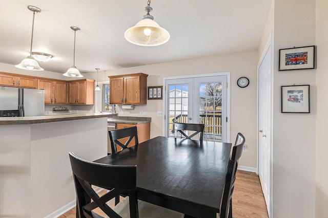 dining area with baseboards, french doors, light wood-style floors, and a healthy amount of sunlight