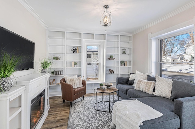 living area featuring an inviting chandelier, crown molding, wood finished floors, and a glass covered fireplace