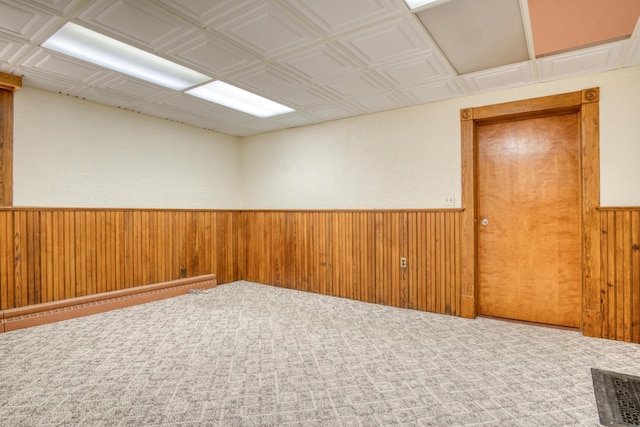 carpeted empty room featuring a baseboard heating unit, visible vents, a wainscoted wall, and wooden walls