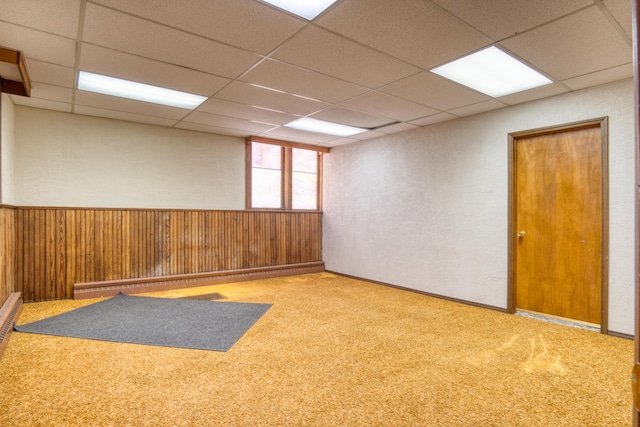 empty room with carpet floors, wood walls, wainscoting, and a paneled ceiling