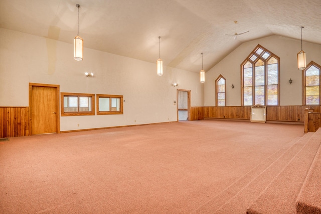 carpeted spare room with high vaulted ceiling, wainscoting, and wood walls