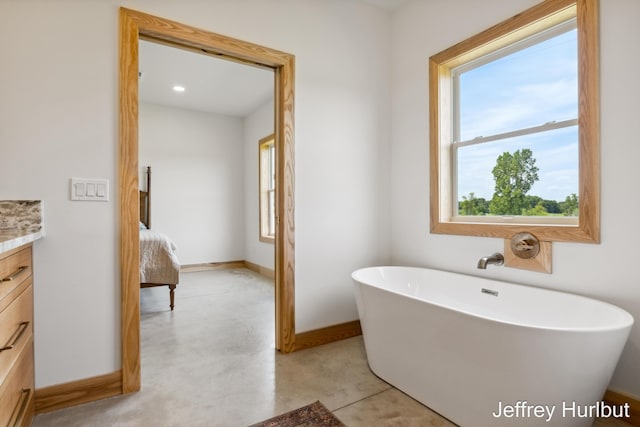 bathroom featuring ensuite bathroom, concrete flooring, a freestanding tub, vanity, and baseboards