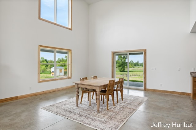 dining space with plenty of natural light, concrete floors, a towering ceiling, and baseboards