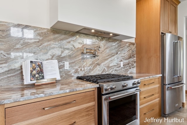 kitchen featuring wall chimney range hood, brown cabinetry, light stone countertops, tasteful backsplash, and high end appliances